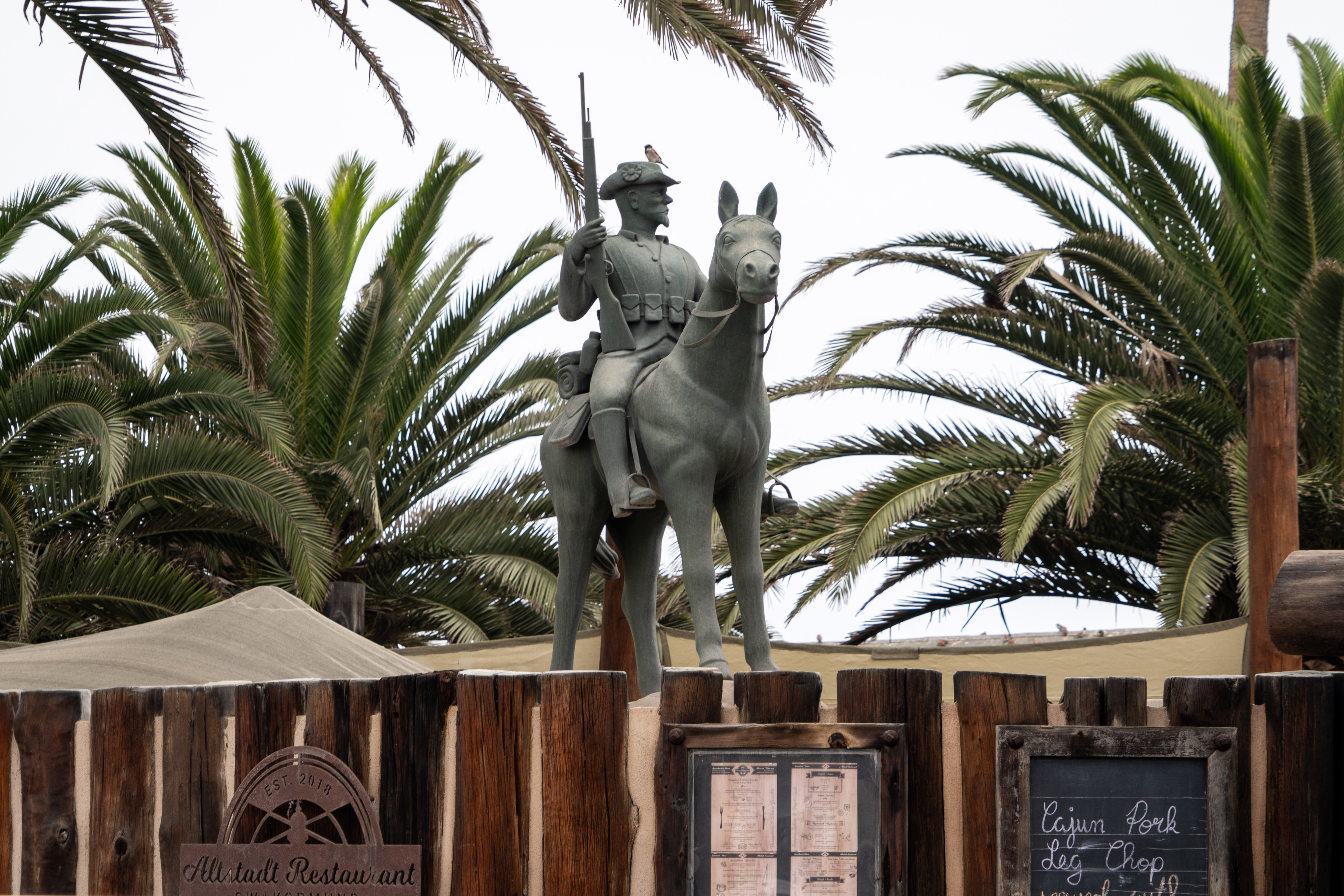 Stinco di maiale, crauti e purè di patate sono nel menu del ristorante Altstadt. Sul basamento si trova una replica del monumento equestre di Windhoek, che commemora i soldati tedeschi caduti tra il 1904 e il 1908.