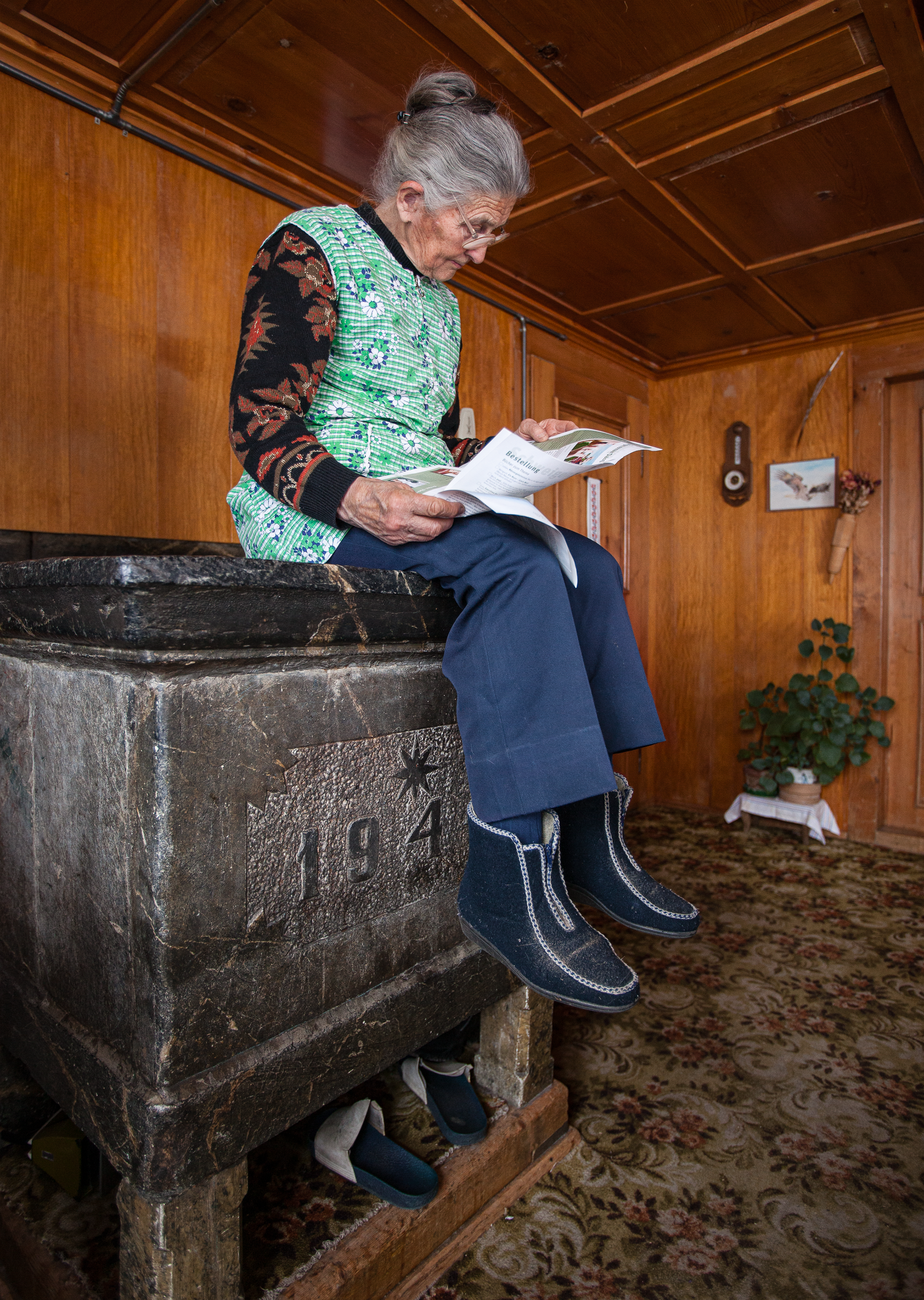 Femme assise sur un poêle en train de lire un journal.