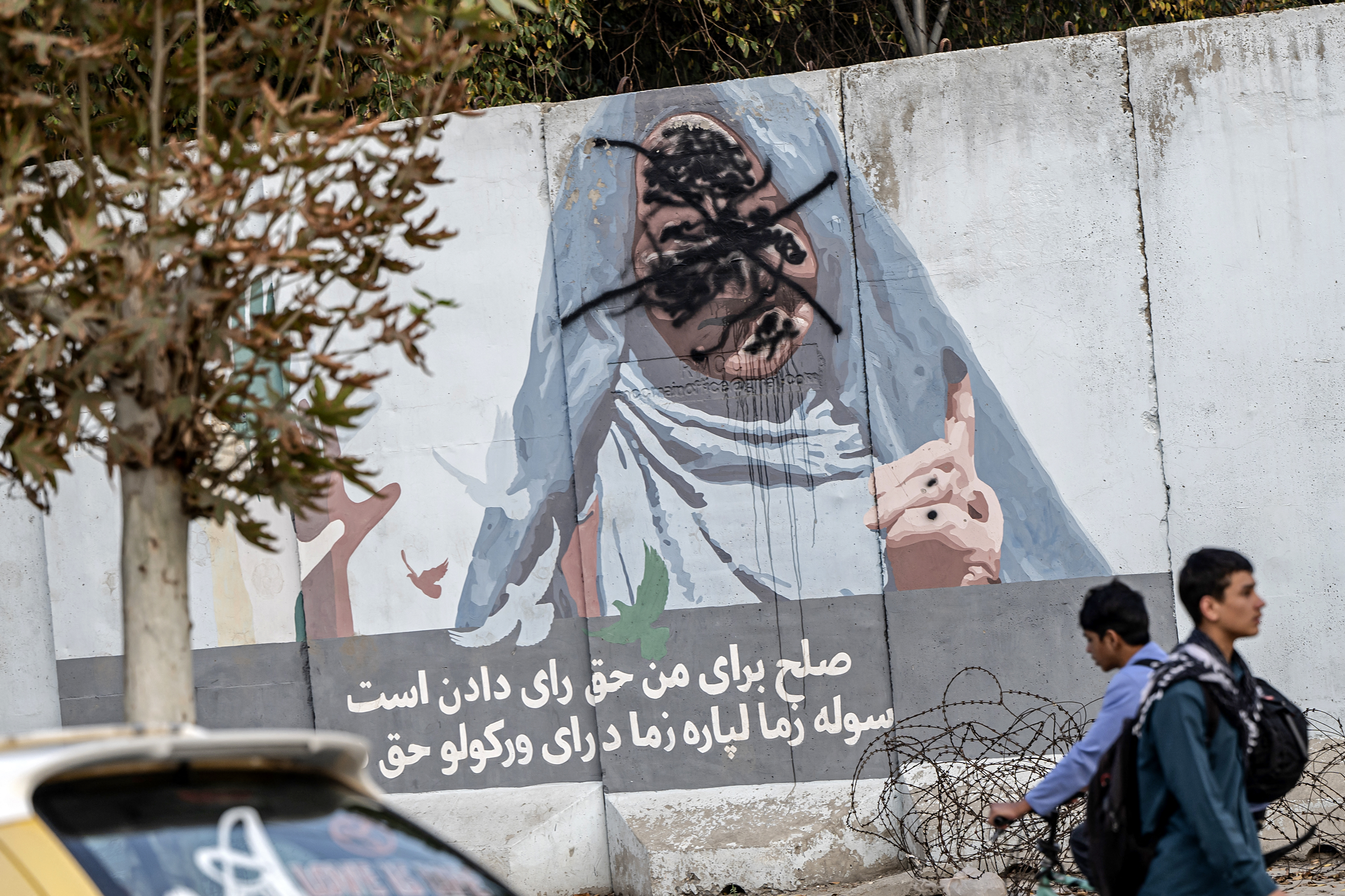 Afghan boys walk past a defaced wall mural reading "Peace for me is the right to vote", along a street in Kabul on Octoer 16, 2024. (Photo by Wakil KOHSAR / AFP)