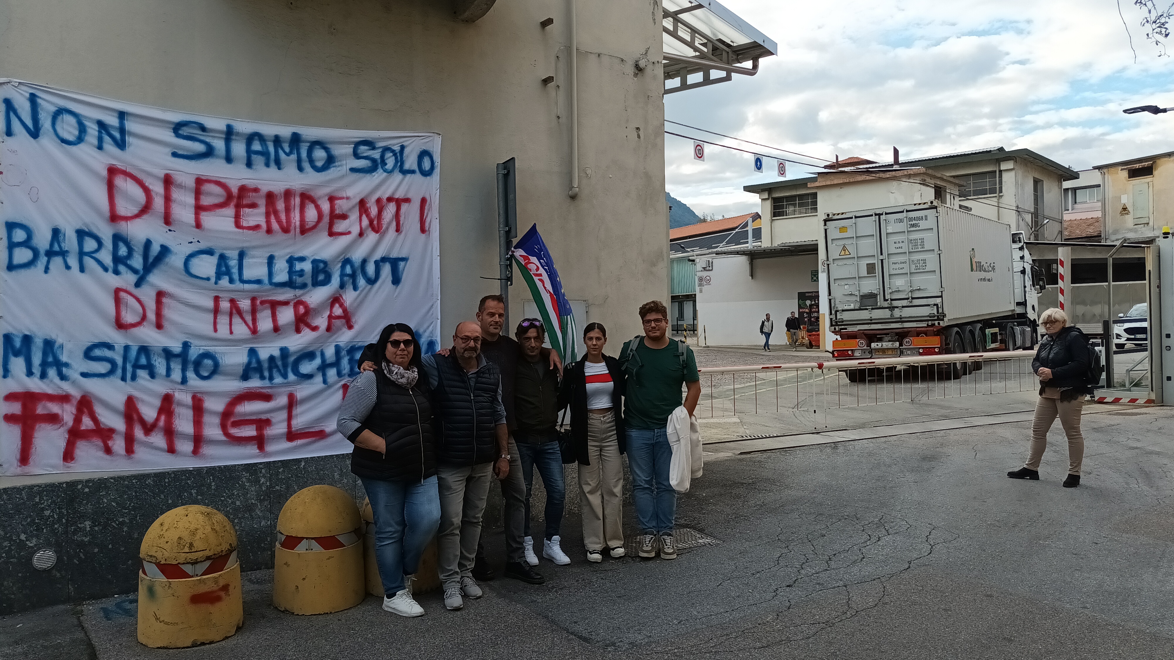 uomini e donne davanti a una fabbrica con uno striscione