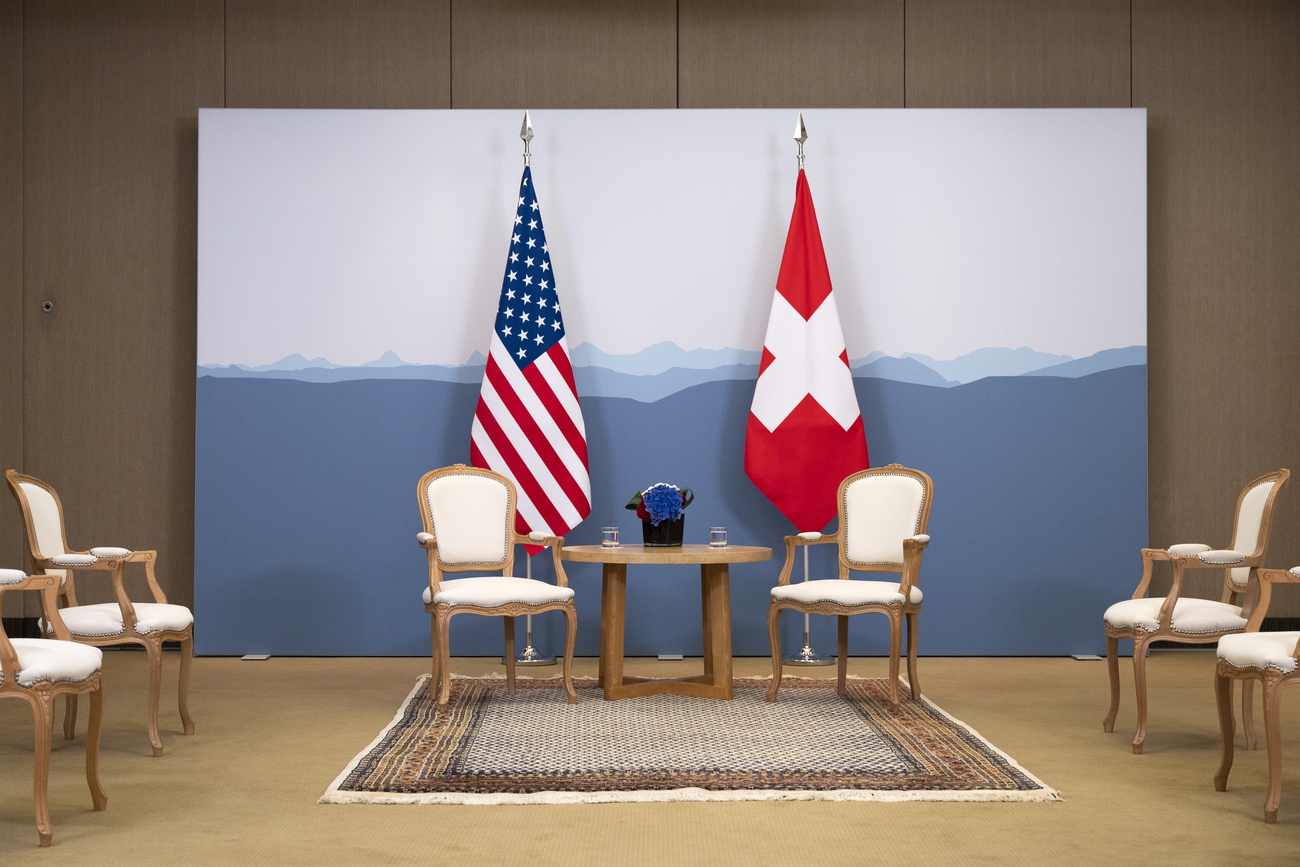 Une table et des chaises vides avec en arrière-fond un drapeau américain et un drapeau suisse.