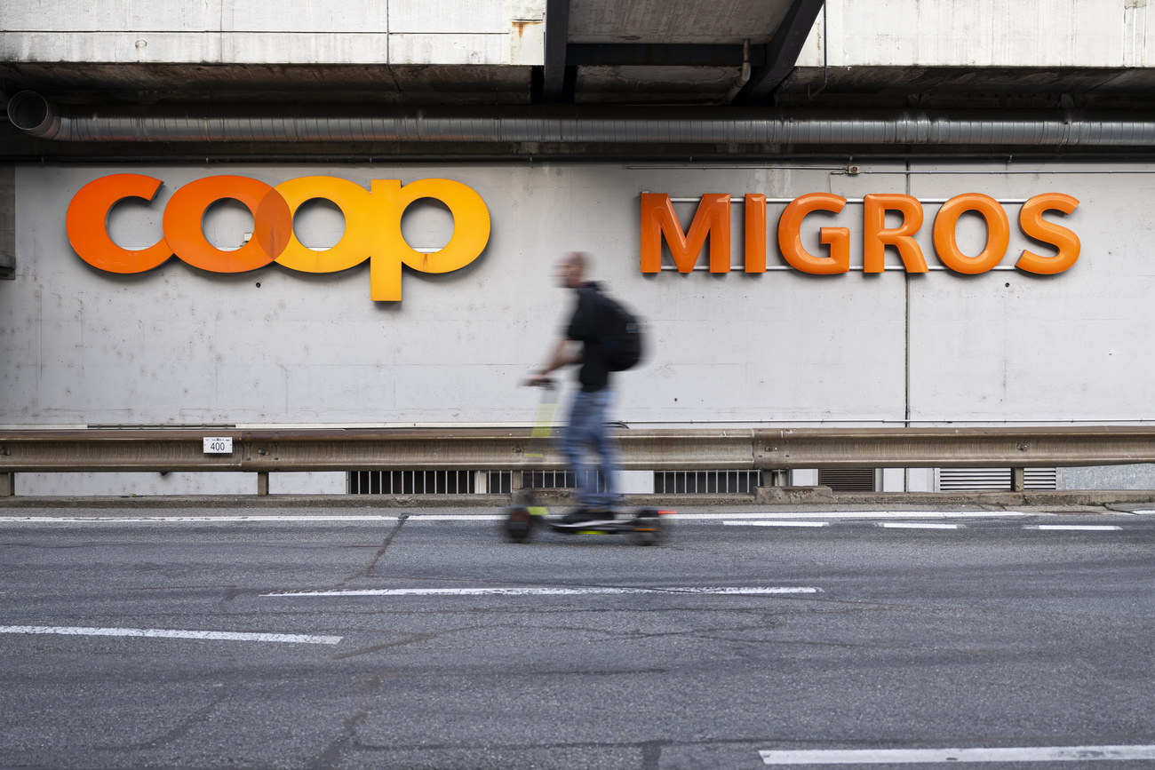 Logos de Coop et de Migros derrière un homme à trotinette.