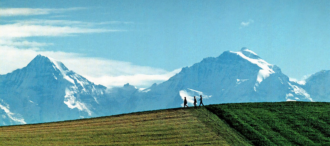 Menschen wandern über ein Feld, Berge im Hintergrund