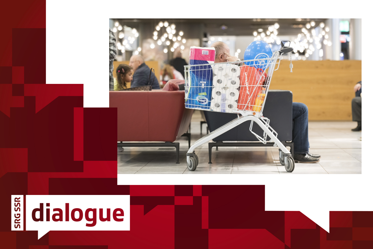 A customer sits behind his full shopping trolley and looks at his mobile phone