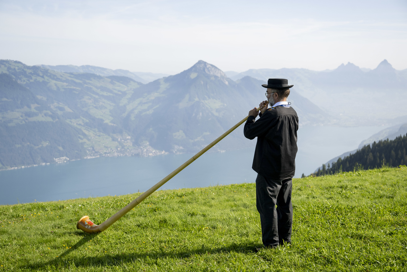 An alphorn player in traditional costume on a meadow overlooking Lake Lucerne.