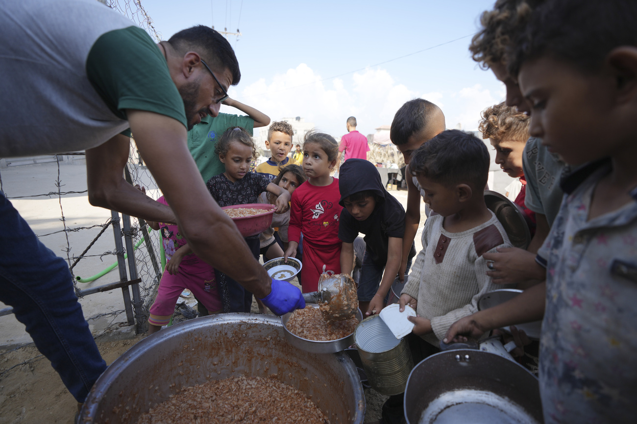 أطفال فلسطينيون نازحون ينتظرون في طابور للحصول على الطعام داخل مخيم في دير البلح بقطاع غزة. 18 أكتوبر 2024.