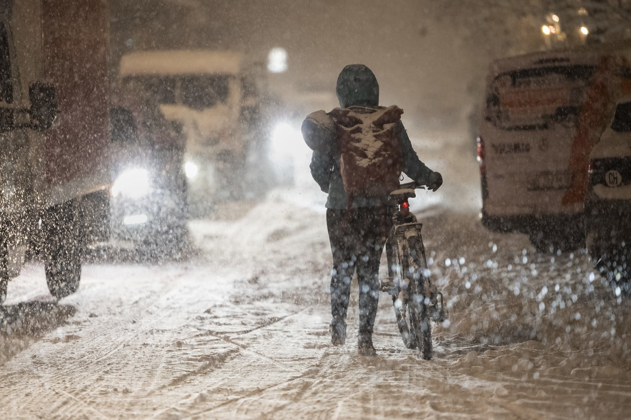 2024年11月21日、大雪に見舞われたベルンのロレーヌ地区。立ち往生する車の横を、自転車を押して通り過ぎる市民