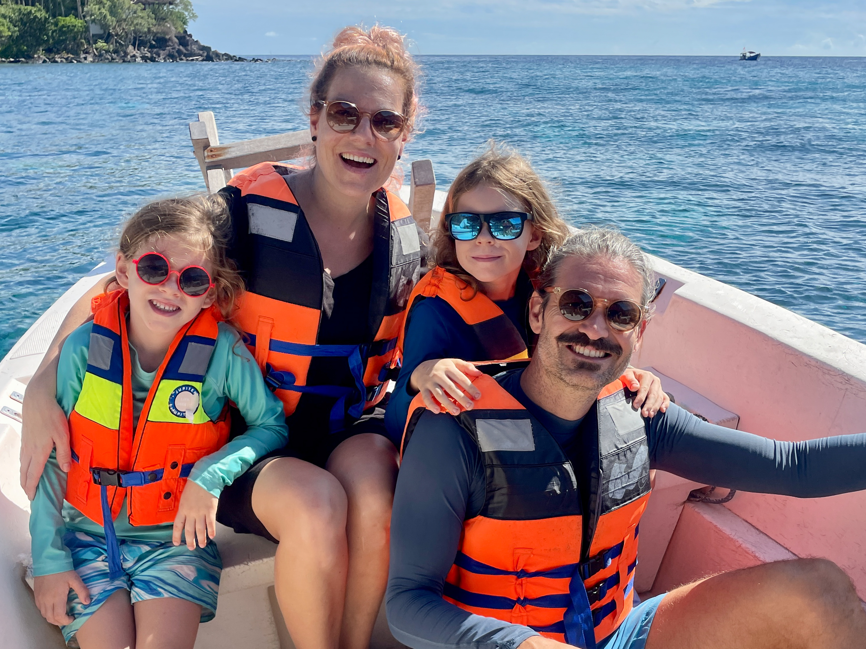 Familie mit Schwimmwesten auf einem Boot mit Meer und Küste im Hintergrund.