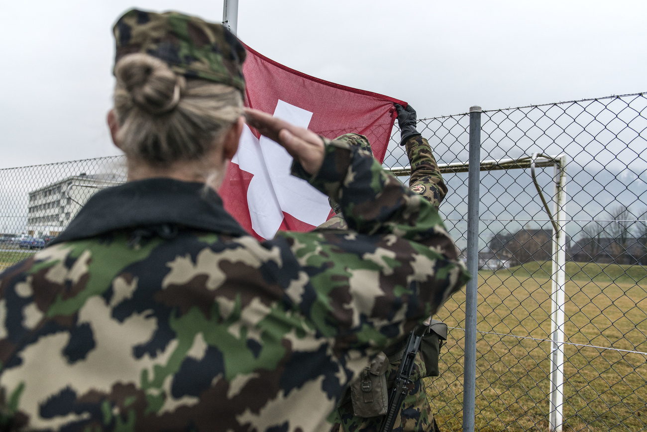 Eine Frau in Kampfuniform grüsst eine Schweizer Flagge