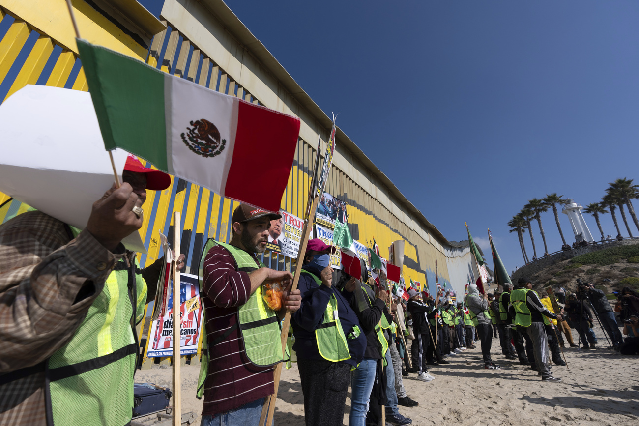 Personas migrantes y activistas ondean banderas mientras realizan una protesta en apoyo a las personas migrantes y solicitantes de asilo cerca del muro fronterizo que separa México y Estados Unidos.