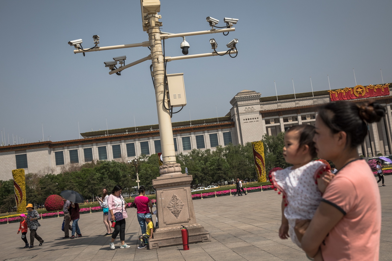 Donna e bambina in piazza Tiananmen passano vicino a telecamere di sorveglianza.