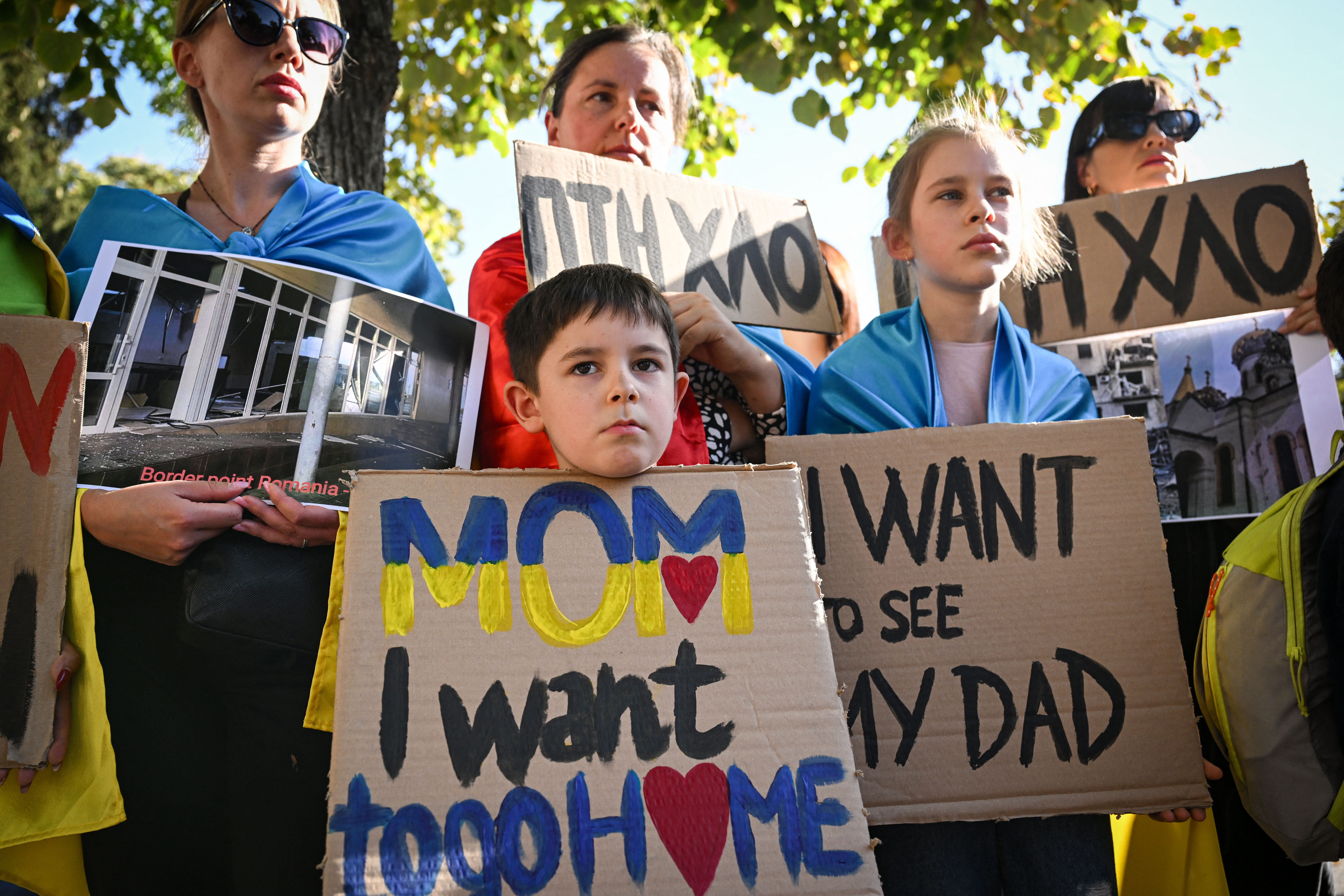 Boy and gilr holding posters that say "Mom I want to go home" and "I want to see my dad"